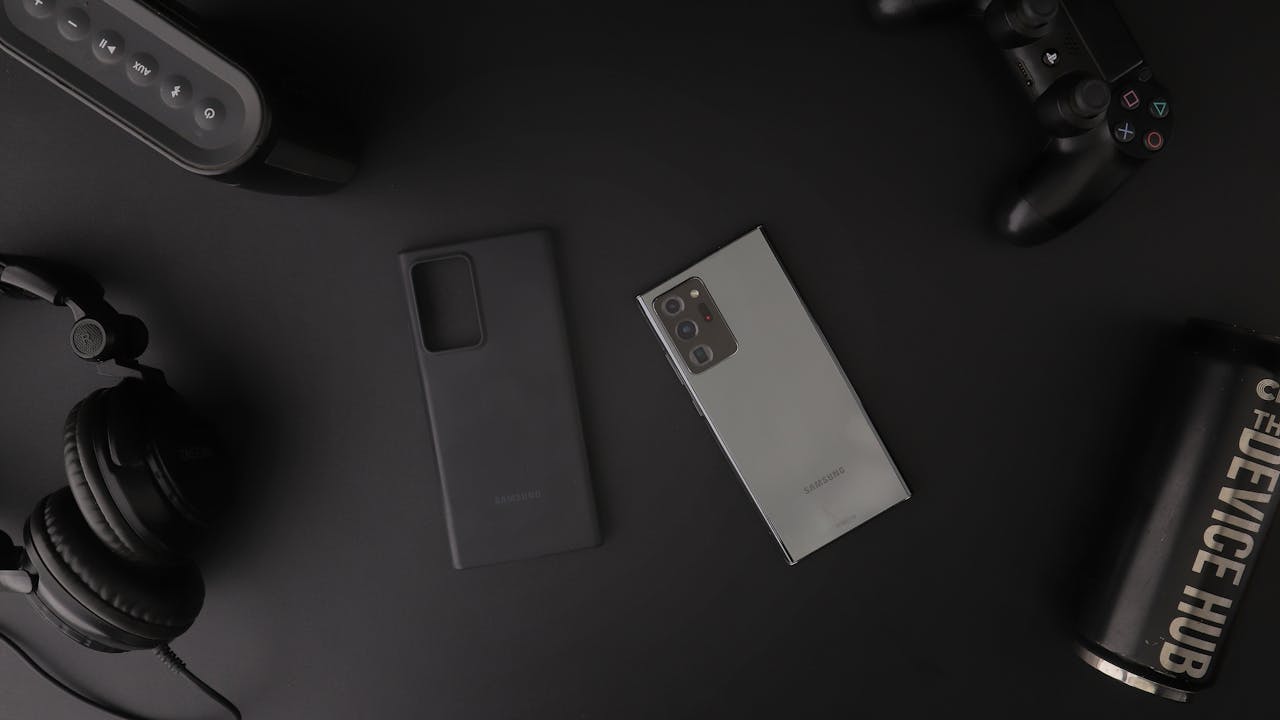 Flat lay of modern electronic gadgets including headphones, phone, and gaming controller on a table.